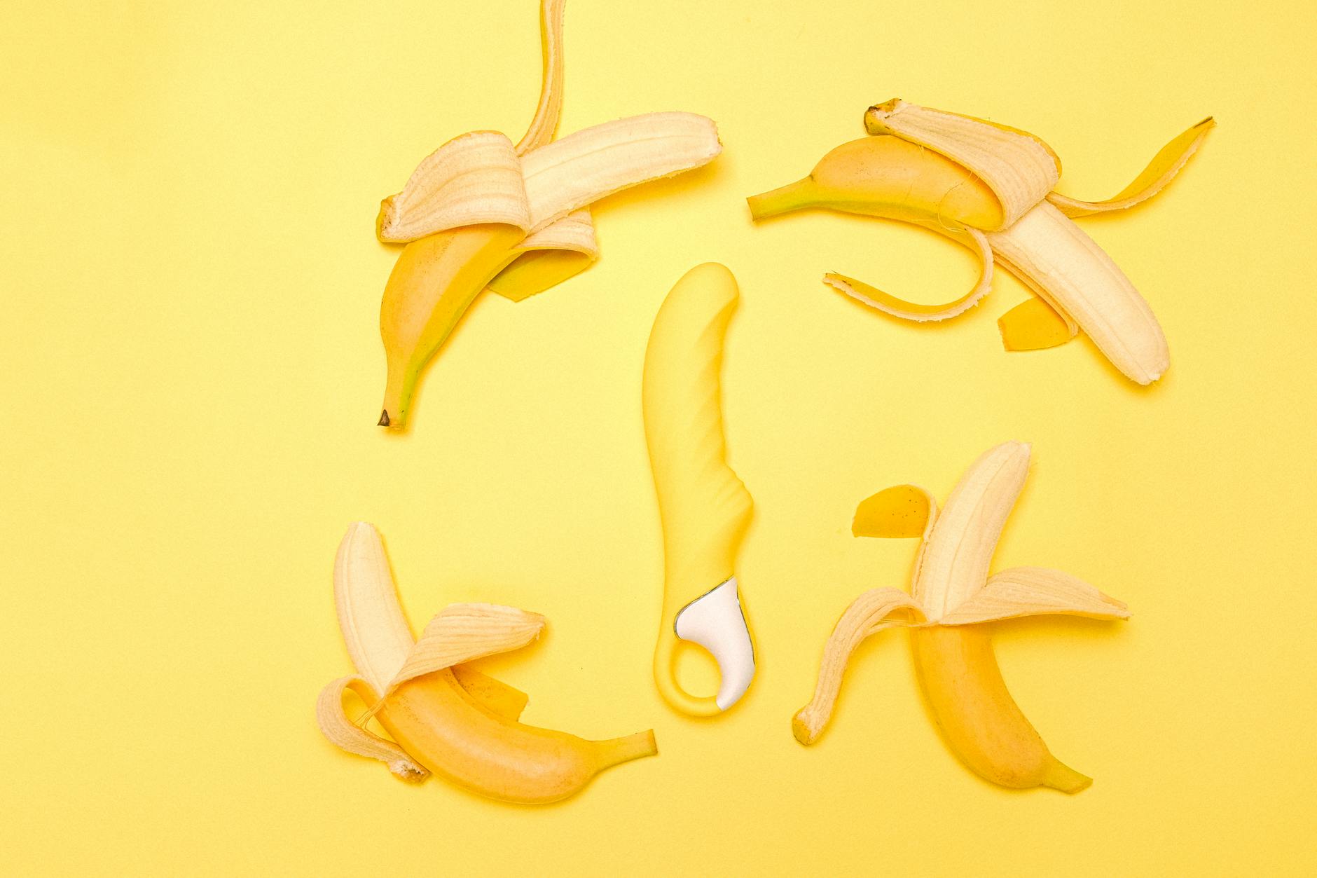 Bright yellow silicone clitoral vibrator surrounded by fresh lemons on a yellow background