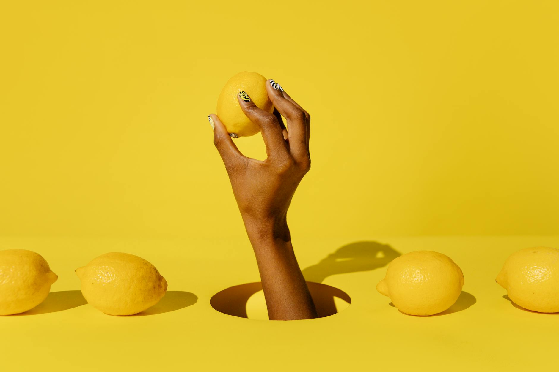 A hand holding a lemon against a vivid yellow background, symbolizing fresh, guilt-free pleasure