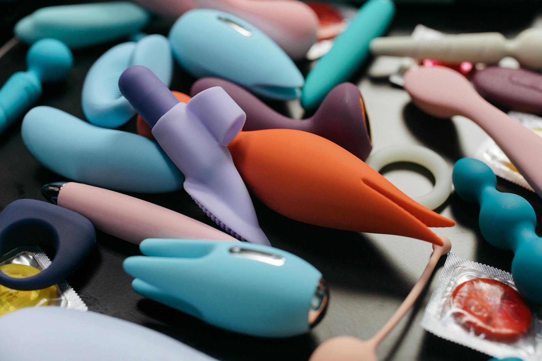 A close-up of a hand holding an orange vibrator against a minimalistic purple backdrop