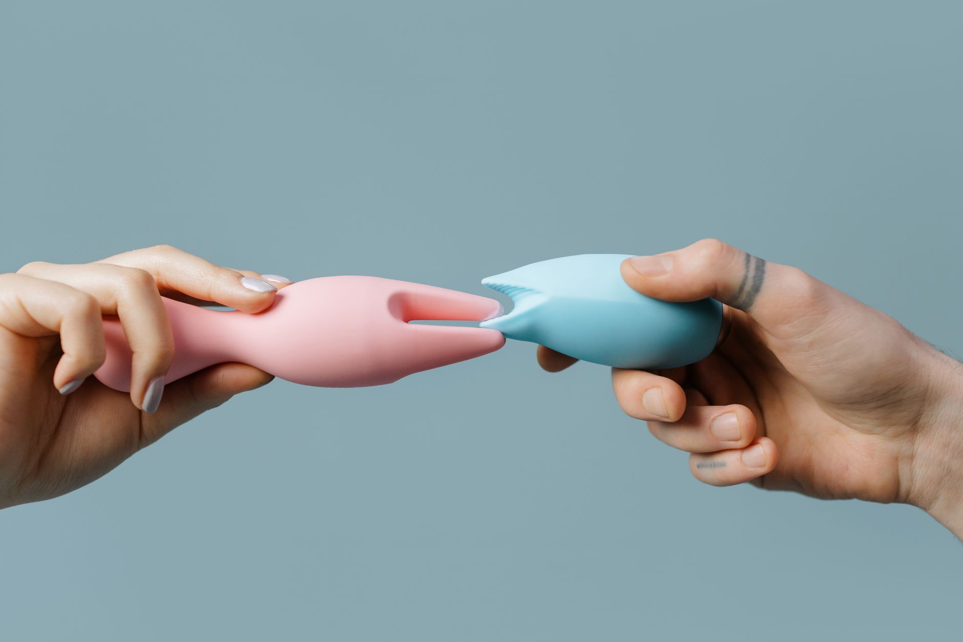 Hands holding colorful silicone vibrators and adult toys on a neutral surface