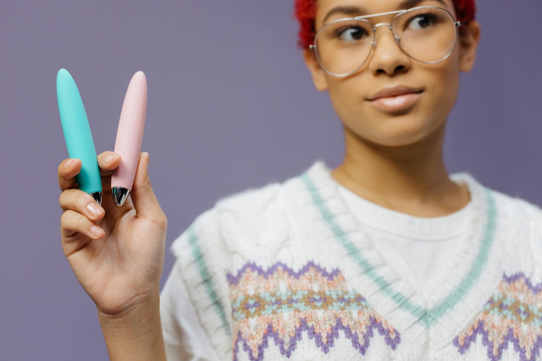 Woman holding two colorful vibrators in a contemplative moment