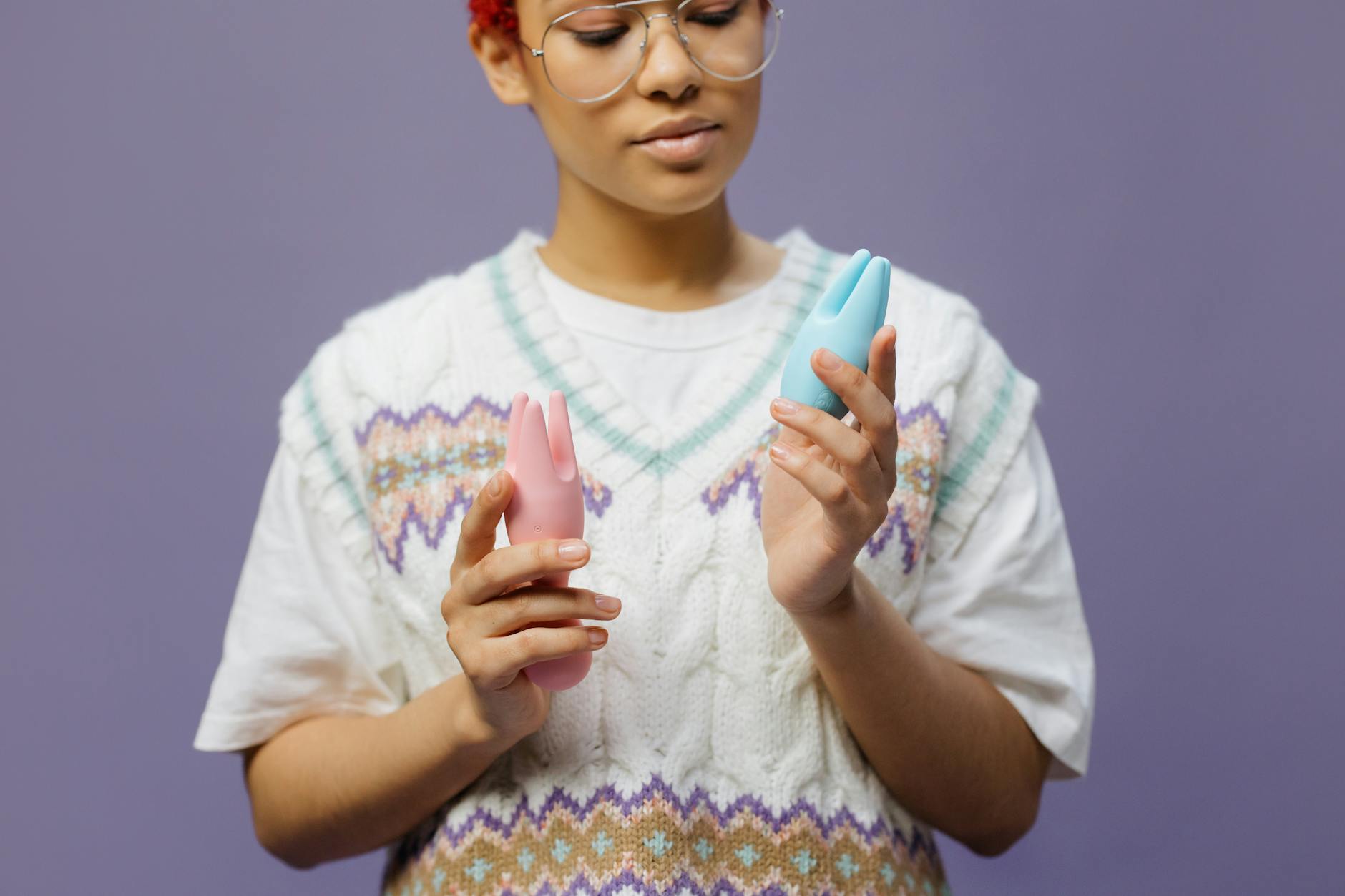 Woman holding blue and pink silicone vibrators with contemplative expression during recovery